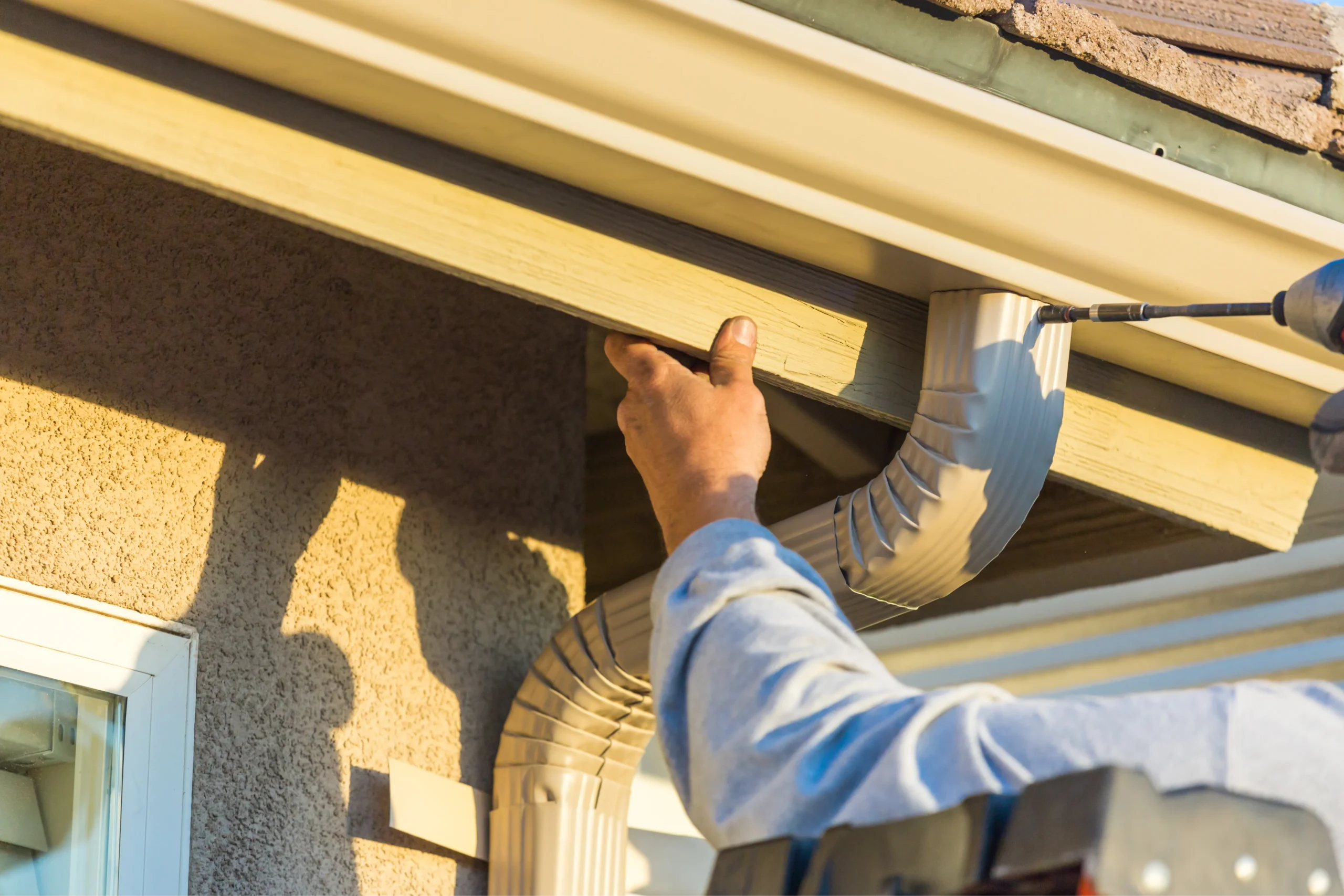 worker attaching aluminum rain gutter and down spout to fascia of house photo 1